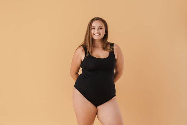 Young woman wearing swimsuit smiling and looking at camera isolated over beige wall - Fotó, kép