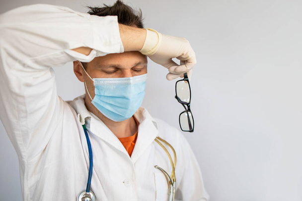 医者の男は、疲れている、疲れや悲しい見て休憩を取る。保護手袋、マスクと聴診器を身に着けている。コロナウイルス｜covid-19の概念 - 写真・画像