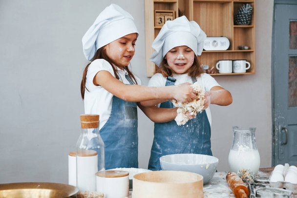 Two little girls in blue chef uniform preparing food on the kitchen. - Foto, Imagen