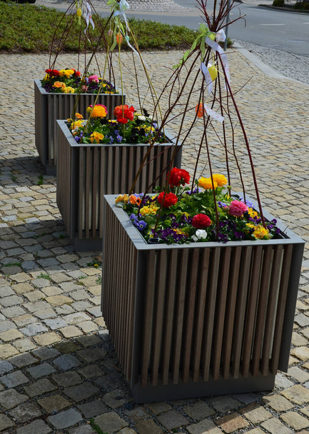 ornamental flower pots on village center trough, wooden flower pots with beautiful decorations of violets and daffodils. Easter is approaching so it is necessary to decorate entrance of home, parking - Photo, Image