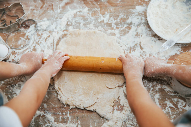 Top view of two little girl's hands that preparing knead by tool on the table. - Foto, Imagen