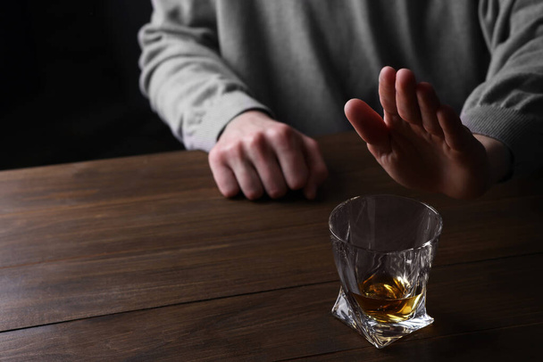 Man refusing to drink whiskey at wooden table, closeup. Alcohol addiction - Фото, зображення