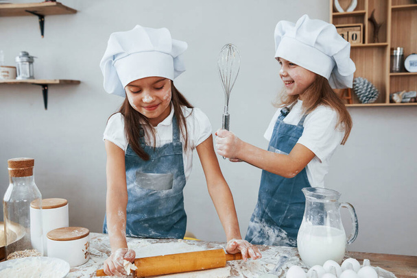 Two little girls in blue chef uniform kneading dough on the kitchen. - Photo, Image