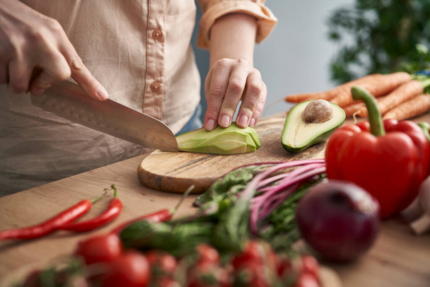 close-up van de handen van de vrouw snijden avocado in de keuken - Foto, afbeelding