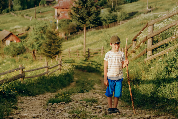 Travel to the mountains in summer. Active holidays with children in the mountains. A boy walks along a dirt road in a village in the summer in the Alpine mountains. - Фото, зображення