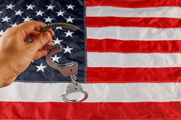 caucasian hand holding silver metal handcuffs over US flag background - Foto, immagini