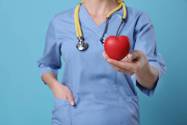 Dokter met stethoscoop en rood hart op lichtblauwe achtergrond, close-up. Cardiologie - Foto, afbeelding