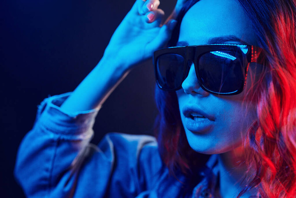 Portrait of young girl in sunglasses in red and blue neon in studio. - Foto, imagen