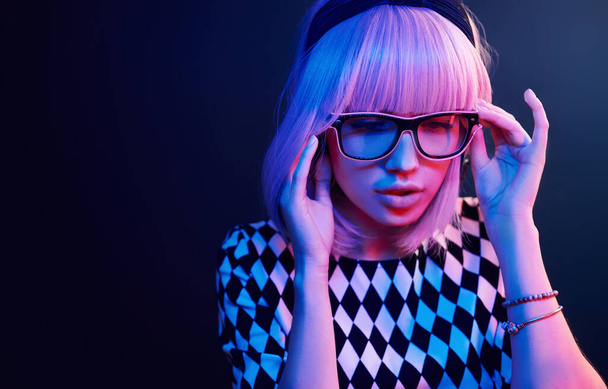 Portrait of young girl with blond hair in eyeglasses in red and blue neon in studio. - Фото, изображение