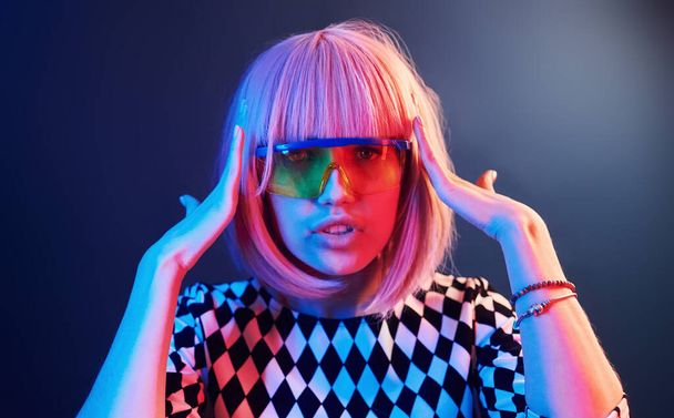 Portrait of young girl with blond hair in eyeglasses in red and blue neon in studio. - 写真・画像