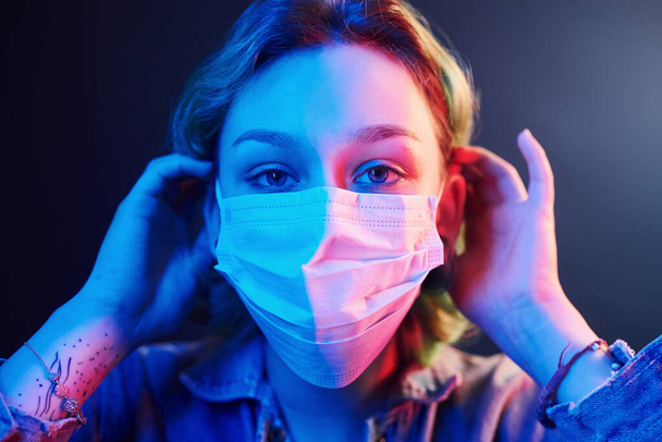 Portrait of girl that wearing protective mask on face in neon lights. - Photo, image