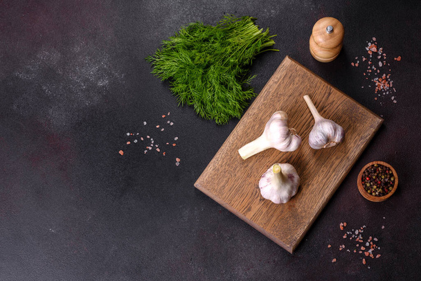 Heads of fresh white garlic on a wooden cutting board against a dark concrete background. Cooking at home - Fotografie, Obrázek