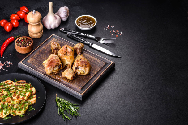 Three chicken legs grilled with spices and herbs on a wooden cutting board against a dark concrete background. Cooking at home - Фото, изображение