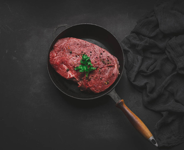 Raw beef tenderloin lies in a metal round frying pan on a black table, top view - Valokuva, kuva