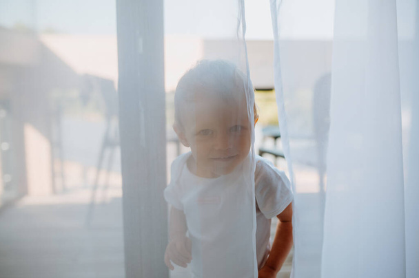 Cute baby girl playing,hiding behind curtains at home. - Foto, imagen