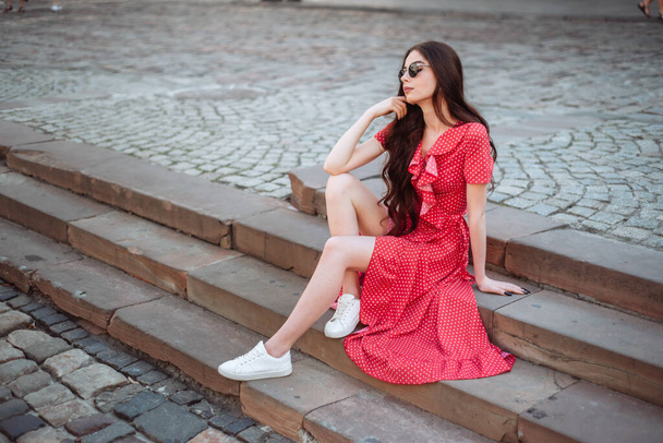 Stílusos lány piros pöttyös ruhában és fehér tornacipőben. fiatal csinos nő nyári szezon portré szabadban - Fotó, kép