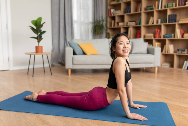 Relief lower back pain. Fit asian lady doing sphinx cobra pose or upward-facing dog asana, stretching back muscles - Foto, Imagem