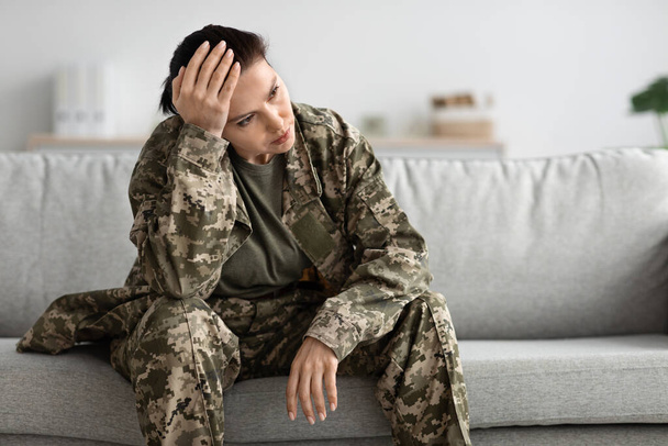 Impacto del Servicio Militar. Deprimida pensativa soldado sentada en un sofá - Foto, imagen