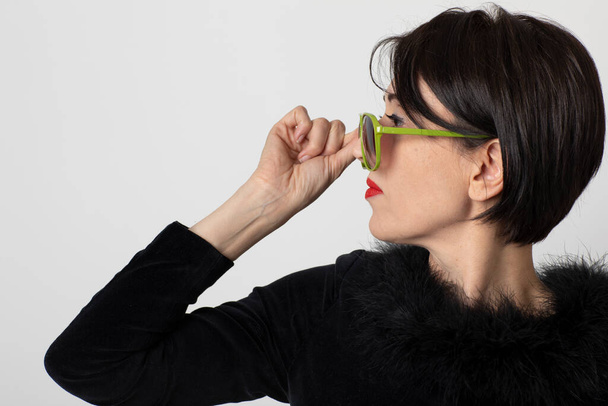 Portrait of elegant woman dressed in black on a white background. Aggressive and provocative profile. She has green sunglasses. - 写真・画像