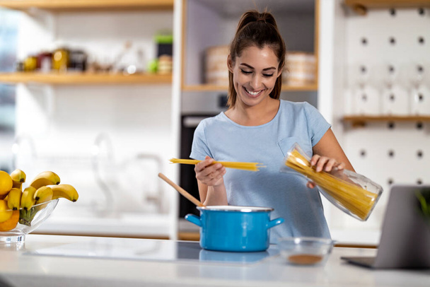 Woman preparing spaghetti in her kitchen at home. - Фото, изображение