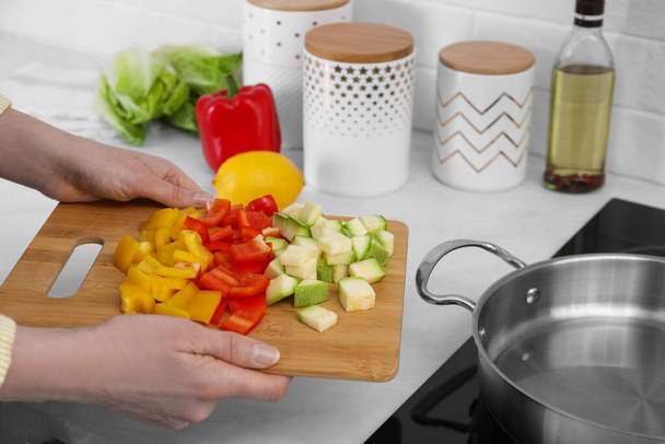 Woman holding wooden board with cut vegetables in kitchen, closeup - Foto, afbeelding
