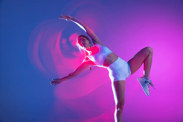 Professional female athlete, runner training isolated on blue studio background in mixed pink neon light. Healthy lifestyle, sport, motion and action concept. - Foto, Bild