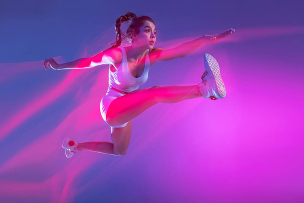 Professional female athlete, runner training isolated on blue studio background in mixed pink neon light. Healthy lifestyle, sport, motion and action concept. - Foto, Imagen