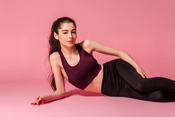 Студийный портрет расслабляющей модели фитнеса в спортивном наряде на розовом фоне. Спорт, здоровый образ жизни - Фото, изображение