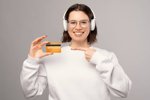 Smiling young cute woman is pointing at a credit card holding she is holding. - Fotó, kép