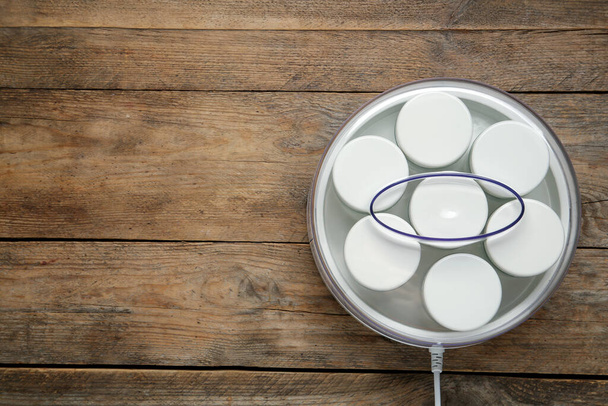 Modern yogurt maker with jars on wooden table, top view. Space for text - 写真・画像