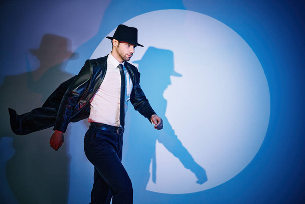 Handsome man in black coat and hat walking like superhero in the spotlight - Fotó, kép