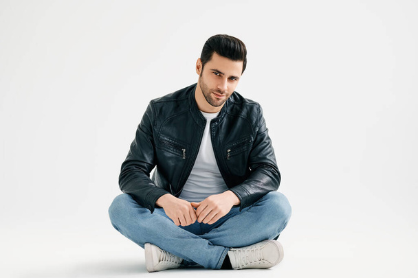 Handsome trendy man sitting on floor isolated on white studio background - Foto, Bild