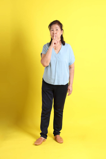 The Asian senior woman wearing light blue shirt standing on the yellow background. - Zdjęcie, obraz