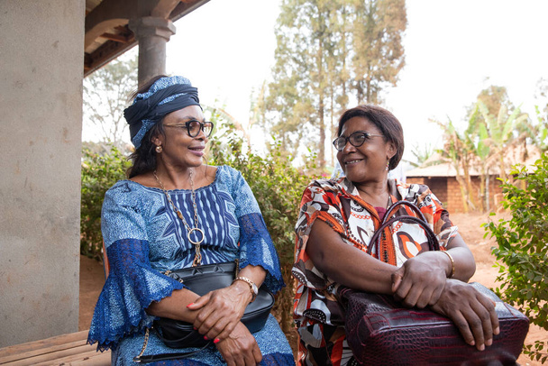 Deux amies africaines âgées sont assises et bavardent, des femmes africaines traditionnellement vêtues ensemble, concept d'amitié adulte - Photo, image
