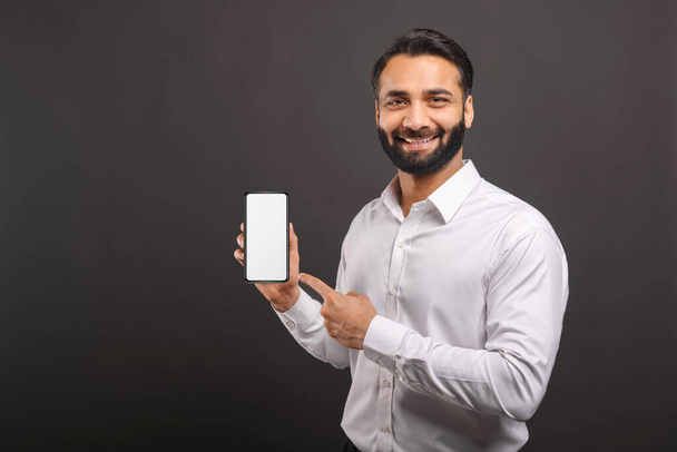 Mock-up concept. Handsome confident bearded Indian man in formal wear showing smartphone with empty screen - Zdjęcie, obraz