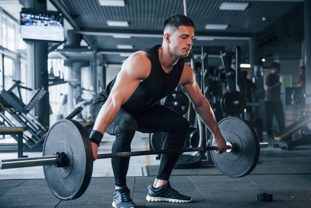 Strong young man in sportive clothes doing exercises with heavy weights in the gym. - Fotoğraf, Görsel