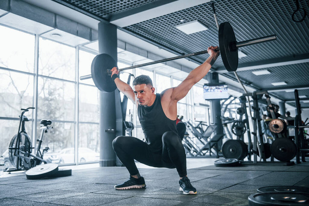 Strong young man in sportive clothes doing exercises with heavy weights in the gym. - Foto, Bild
