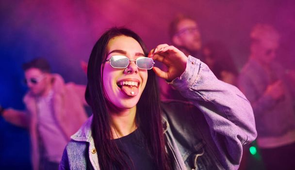 Young girl holding drug pills on togue in front of young people that having fun in night club with colorful laser lights. - Foto, Imagem