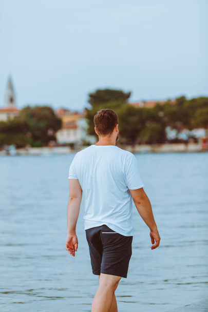 man walking by sea beach in summer evening fazana town on background in croatia. vacation concept - Photo, Image