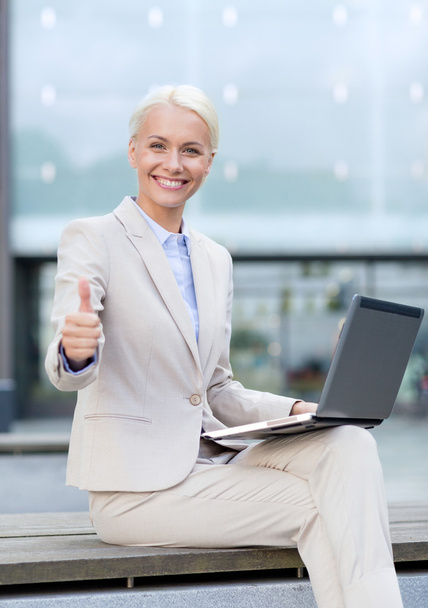 smiling businesswoman working with laptop outdoors - Fotó, kép