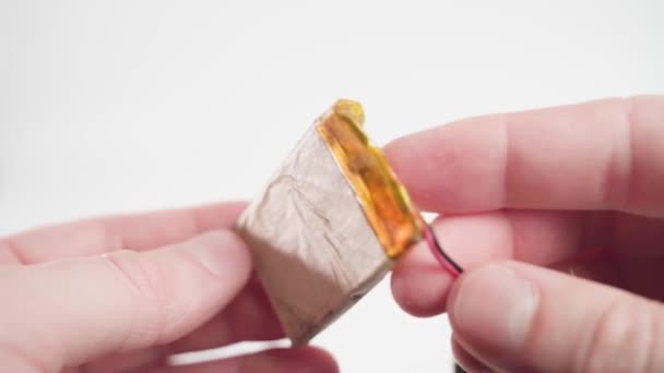 Dünne alte Lithium-Polymer-Batterie in einer Papierhülle mit einer elektronischen Leiterplatte in Nahaufnahme in den Händen auf weißem Hintergrund - Filmmaterial, Video