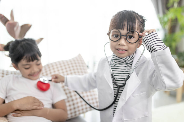 Two cute children play doctor and hospital using stethoscope. Friends girls having fun at home or preschool. - Photo, image