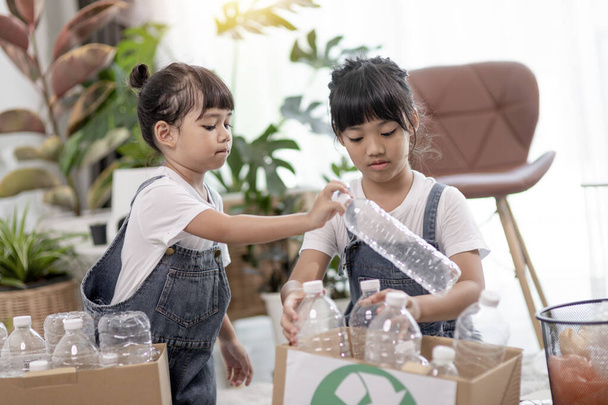 Lächelnde Kinder haben Spaß, während sie Plastikflaschen und Papier in einen Mülleimer werfen - Foto, Bild