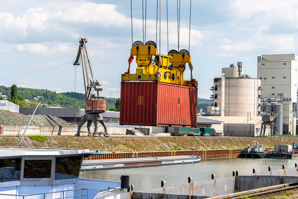 Una grúa de pórtico de contenedores sobre un riel carga el contenedor en una barcaza a orillas del río Rin en Alemania. - Foto, Imagen