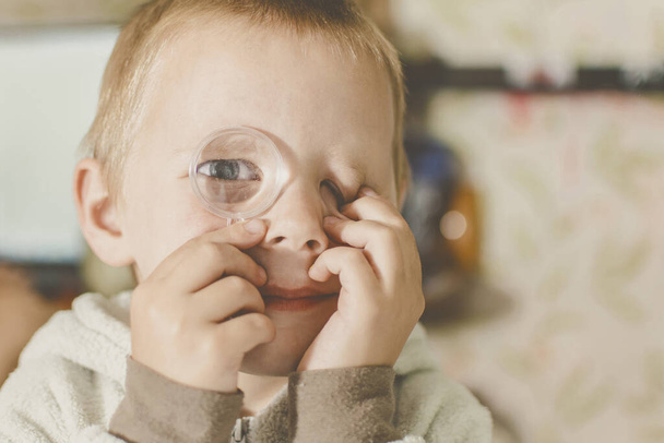 A little boy looks into a magnifying glass. - Fotó, kép