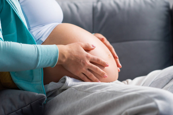 Junge schwangere Frau ruht sich zu Hause aus und erwartet ein Baby. Schwangerschaft, Mutterschaft, Gesundheitsfürsorge und Lebensstil-Konzept. - Foto, Bild