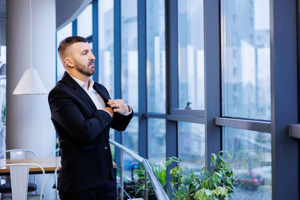 Adult male businessman, teacher, mentor looks out the large window of his office. Work in the office. Development of a new business project - Фото, зображення