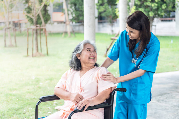 Asian doctor woman, attractive and young, looking and taking care elderly woman patient with paralysis, is sitting on a wheelchair, to elderly patient and health care concept. - Foto, Bild