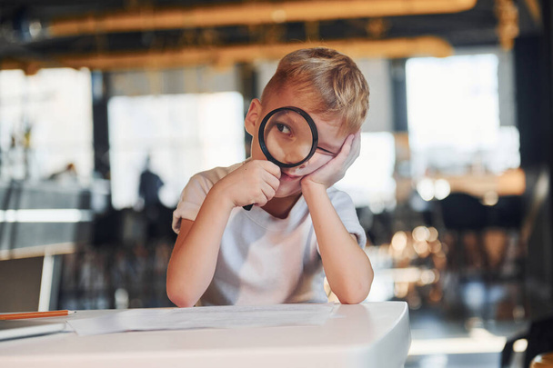 Smart child in casual clothes with laptop on table have fun with magnifying glass. - Foto, Imagem