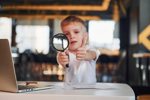 Smart child in casual clothes with laptop on table have fun with magnifying glass. - Foto, Imagen